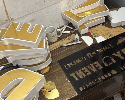 Goudkleurige 3D-letters worden geassembleerd op de werkbank van ALFA Signage